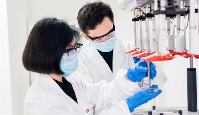 Two scientists wearing masks and gloves work on an analytical instrument, ensuring precision for quality control in pharmaceutical development.