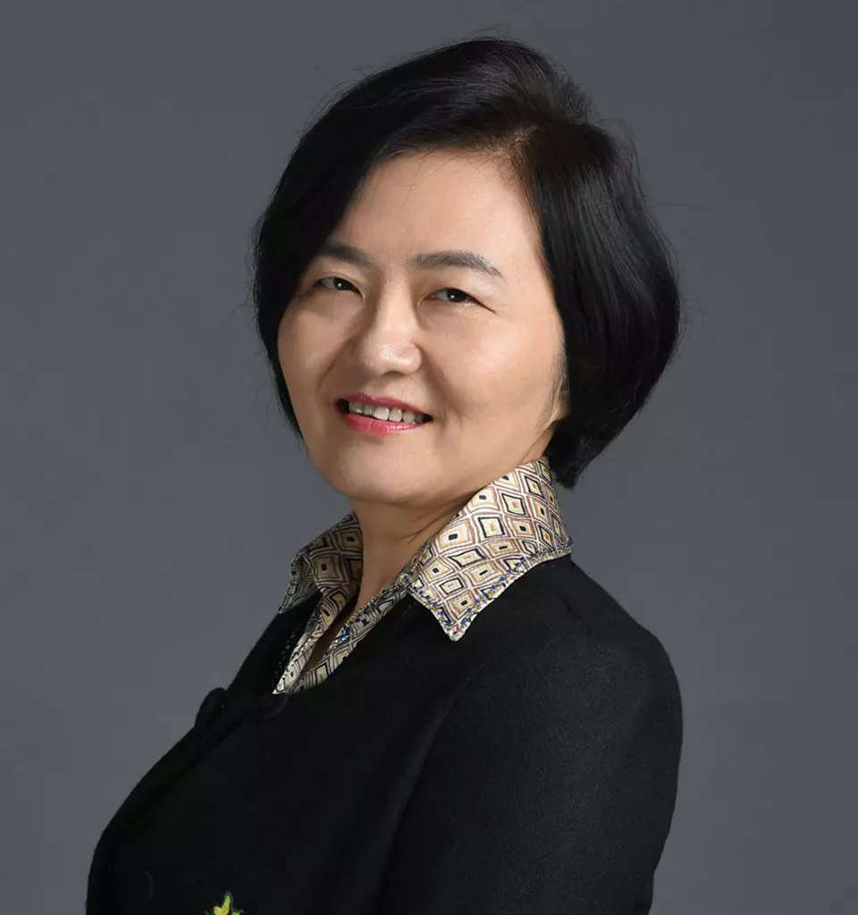 Bei Zheng - A woman with short black hair, wearing a black blazer over a patterned collared shirt, smiles at the camera. The background is a neutral gray, adding a touch of professionalism to her expertise in genetic toxicology.