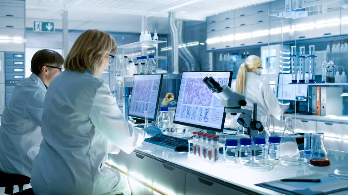 cientists in a modern laboratory analyze ocular safety data on dual monitors, surrounded by test tubes, microscopes, and lab equipment.