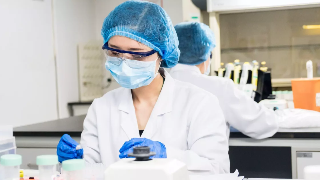 A scientist in protective gear conducts safety pharmacology assessments, carefully handling test tubes and samples in a laboratory environment.