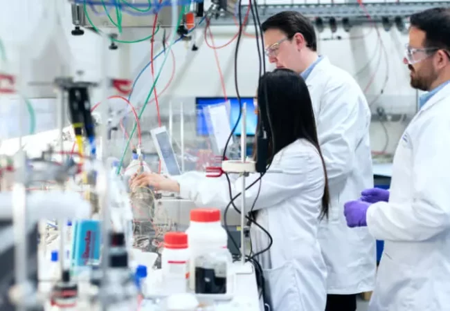 Three scientists work at a lab bench filled with equipment and tubing, conducting permeability studies with various chemicals and instruments in use.