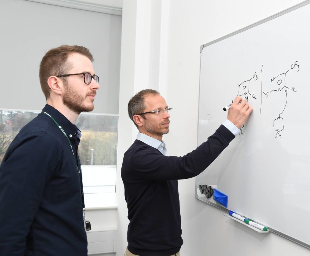 Two men at a whiteboard discussing medicinal chemistry