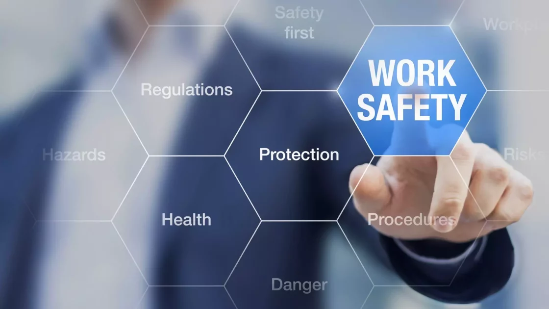 A person is touching a blue hexagon labeled "Work Safety" on a digital interface with surrounding hexagons labeled "Regulations," "Protection," "Health," "Hazards," "Safety first," and more, all crucial for bioanalytical development. The background is blurred.