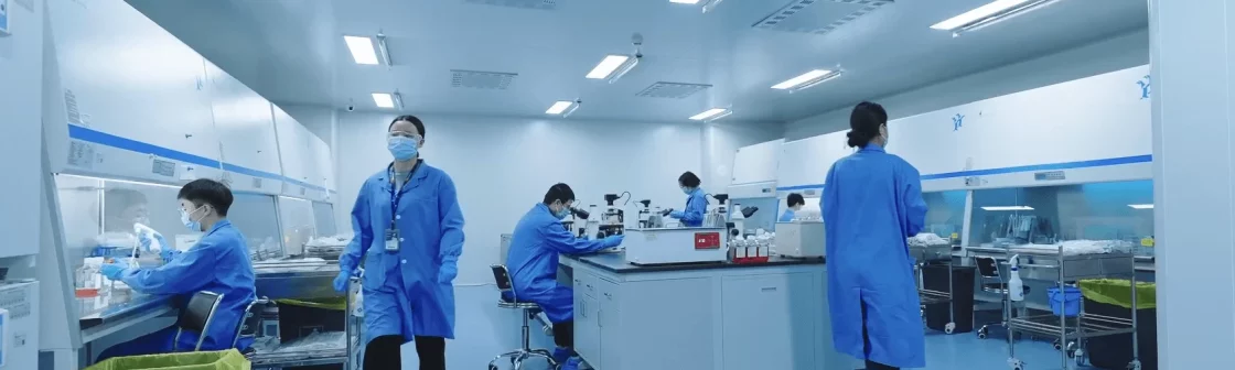Scientists in blue lab coats and masks work inside a sterile cell culture room, performing tasks related to cell line engineering at various workstations.