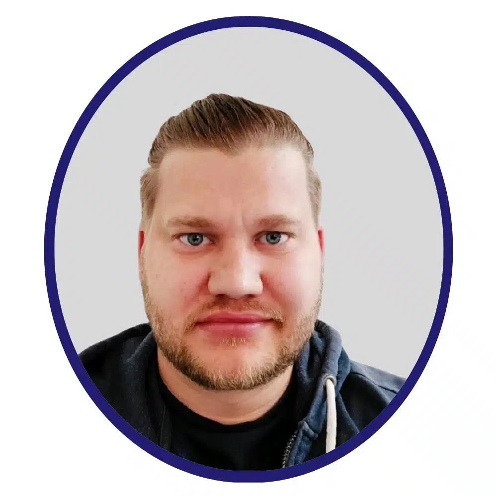Professional headshot of a man with short, slicked-back hair and a beard, wearing a dark hoodie, framed within a circular border on a neutral background.