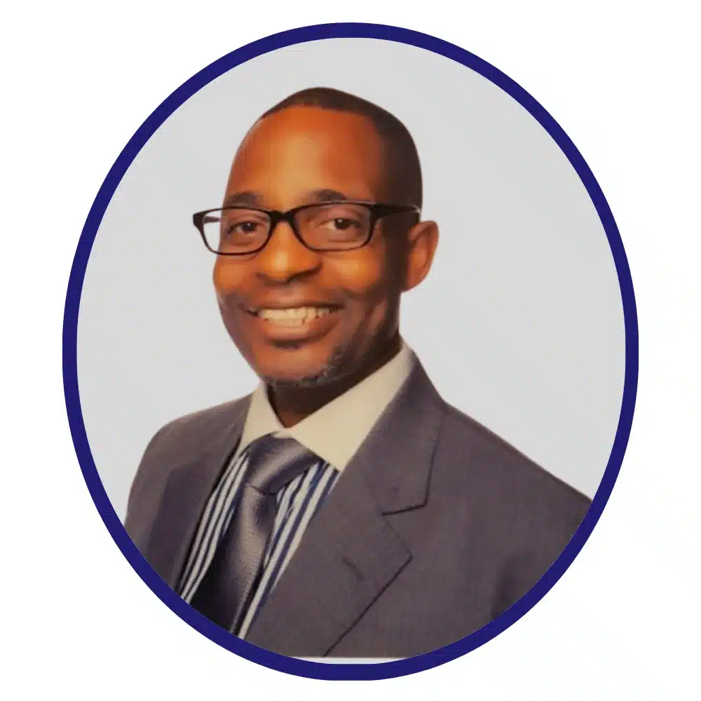 Professional headshot of a smiling man with glasses, wearing a dark suit, white shirt, and striped tie, framed within a circular border on a neutral background.