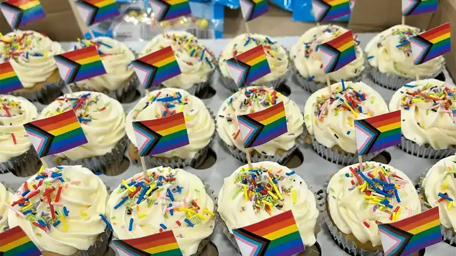Cupcakes topped with rainbow sprinkles and mini Progress Pride flags for a Pharmaron pride celebration.