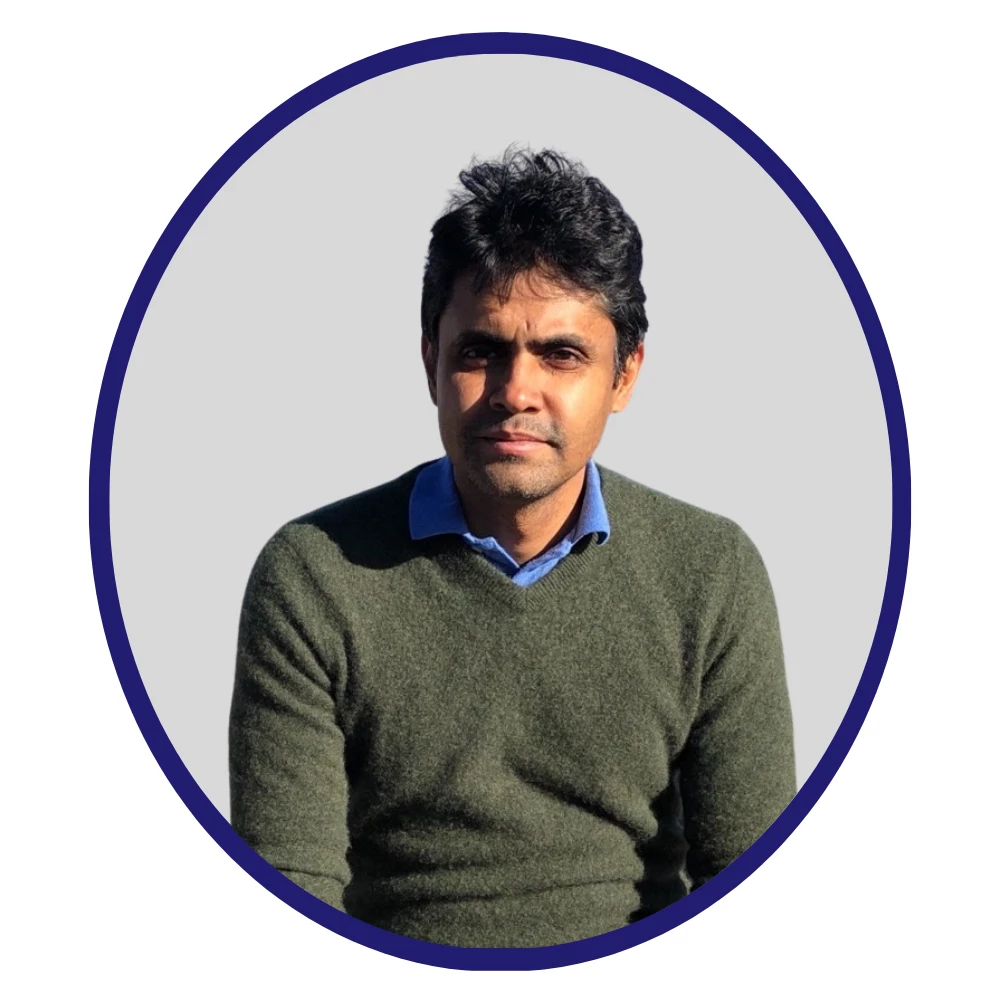 Scientist wearing a green sweater over a blue collared shirt, posed against a light grey background within a dark blue oval frame.