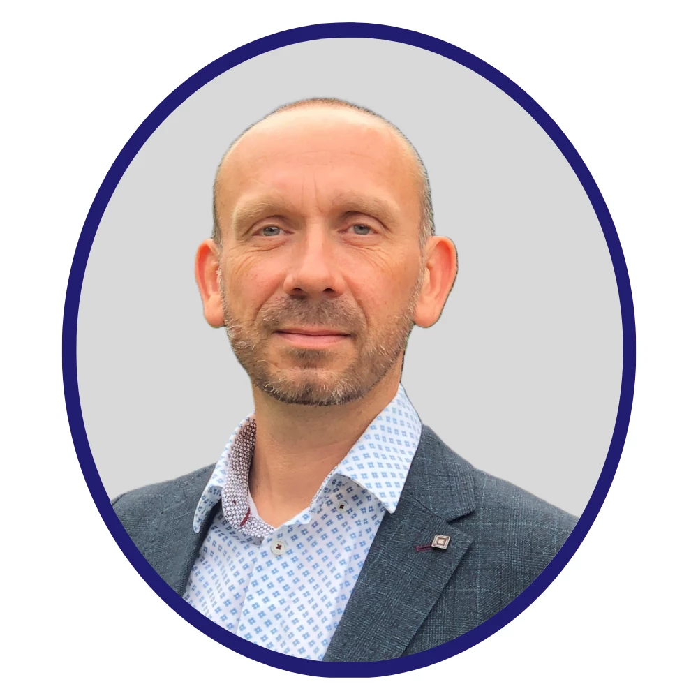 Balding male scientist in a patterned shirt and blazer, facing forward with a neutral expression, set against a light grey background with blue border.