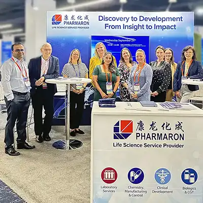 Pharmaron scientists at a conference booth promoting life science services from discovery to development, standing in front of branded display materials.