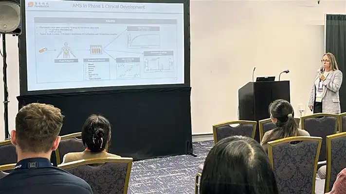 Scientist presenting on AMS in Phase 1 clinical development to an audience at a conference, with a slide projected on a large screen.