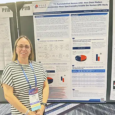 Scientist standing beside a Pharmaron research poster on ¹⁴C-radiolabelled human AME and accelerator mass spectrometry at a scientific conference.