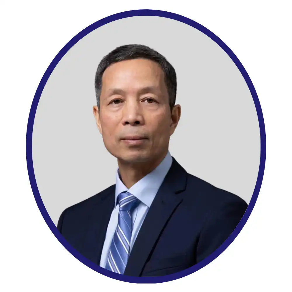 Corporate headshot of scientist in navy suit and blue tie, neutral gray background, oval portrait with blue border.