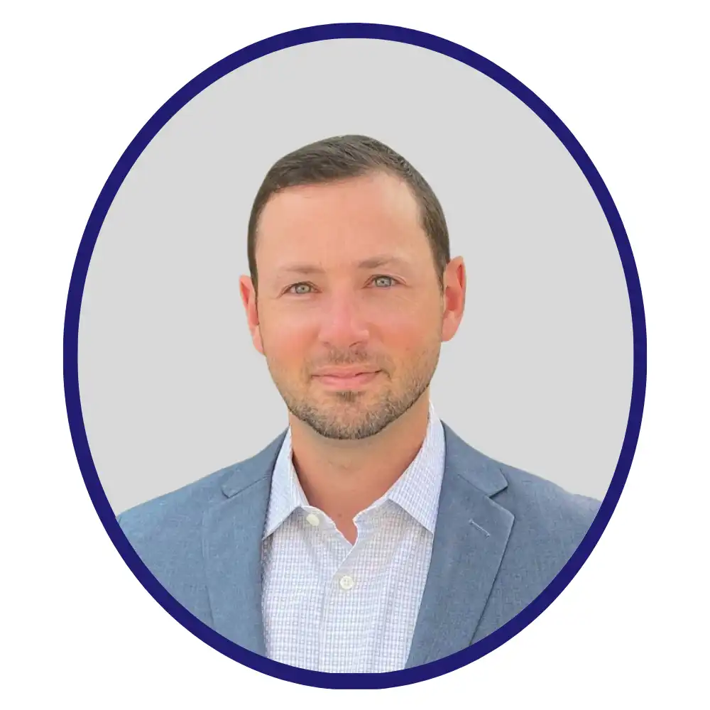 Professional headshot of male scientist in red sweater over blue check shirt, neutral grey background with navy oval border.