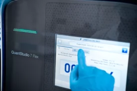 Gloved scientist operating QuantStudio 7 Flex qPCR touchscreen during a CGT analytical testing services experiment