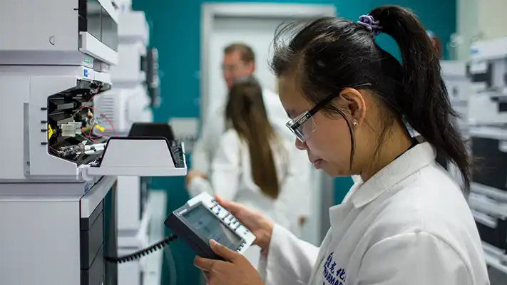 Pharmaron scientist operates an HPLC system with a handheld controller as colleagues work nearby, illustrating CGT regulatory guidance